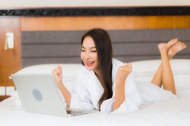 Retrato hermosa joven asiática usar computadora portátil en la cama en el interior del dormitorio