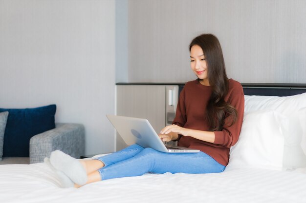 Retrato hermosa joven asiática usar computadora portátil en la cama en el interior del dormitorio