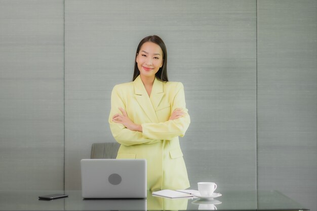 Retrato hermosa joven asiática usar computadora portátil con teléfono móvil inteligente en la mesa de trabajo en la habitación interior