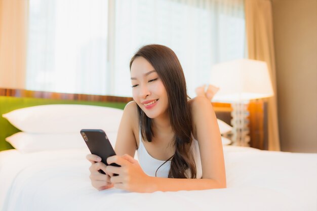 Retrato hermosa joven asiática usar teléfono móvil inteligente en la cama en el interior del dormitorio