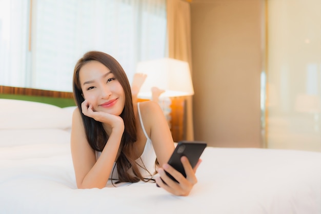 Retrato hermosa joven asiática usar teléfono móvil inteligente en la cama en el interior del dormitorio