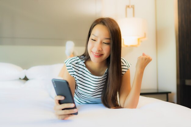 Retrato hermosa joven asiática usar teléfono móvil inteligente en la cama en el interior del dormitorio