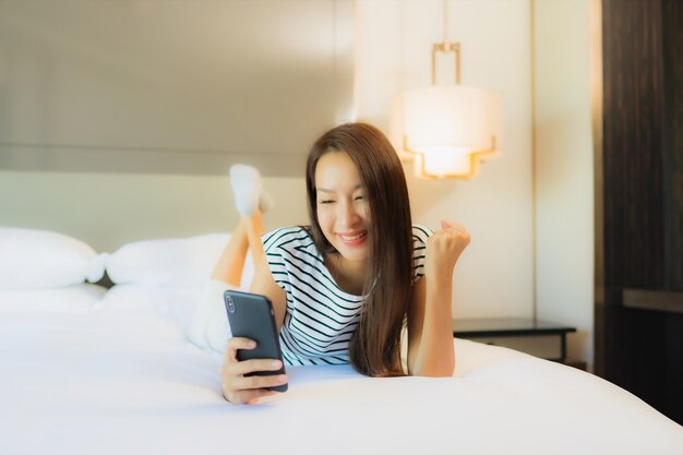 Retrato hermosa joven asiática usar teléfono móvil inteligente en la cama en el interior del dormitorio