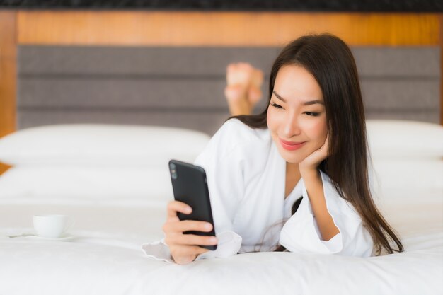 Retrato hermosa joven asiática usar teléfono móvil inteligente en la cama en el interior del dormitorio