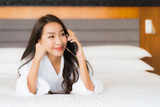 Retrato hermosa joven asiática usar teléfono móvil inteligente en la cama en el interior del dormitorio