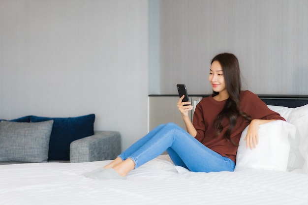 Retrato hermosa joven asiática usar teléfono móvil inteligente en la cama en el interior del dormitorio