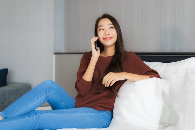 Retrato hermosa joven asiática usar teléfono móvil inteligente en la cama en el interior del dormitorio