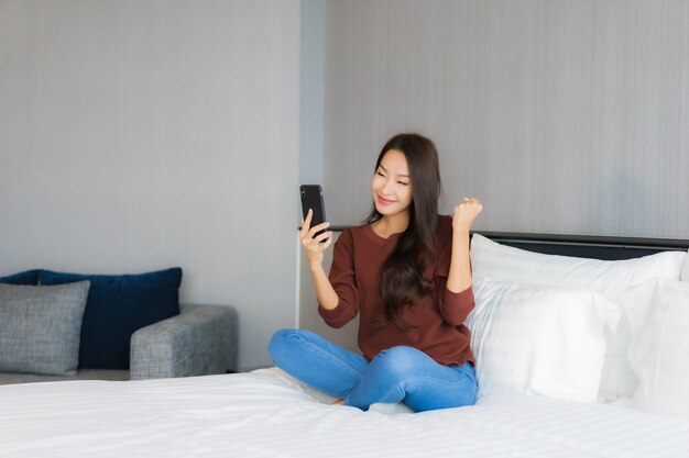 Retrato hermosa joven asiática usar teléfono móvil inteligente en la cama en el interior del dormitorio