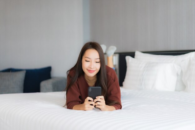 Retrato hermosa joven asiática usar teléfono móvil inteligente en la cama en el interior del dormitorio