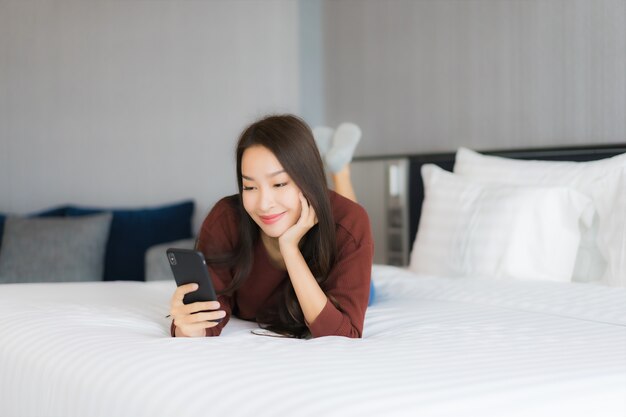 Retrato hermosa joven asiática usar teléfono móvil inteligente en la cama en el interior del dormitorio