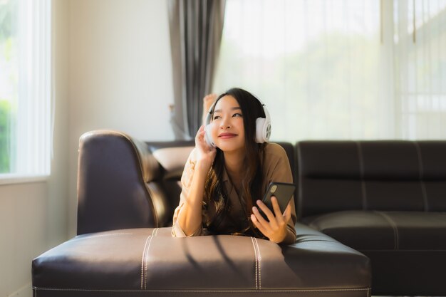 Retrato hermosa joven asiática utiliza teléfono inteligente en el sofá con auriculares