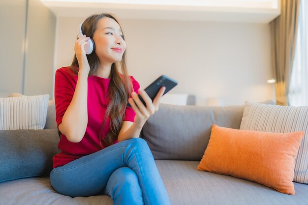 Retrato hermosa joven asiática utiliza teléfono móvil inteligente con auriculares para escuchar música