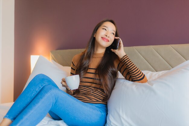 Retrato hermosa joven asiática utilizar teléfono móvil inteligente en la cama