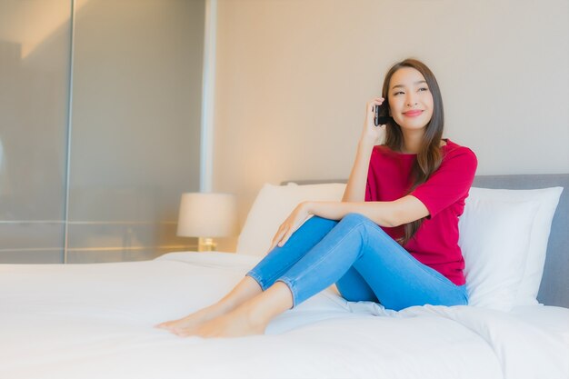 Retrato hermosa joven asiática utilizar teléfono móvil inteligente en la cama