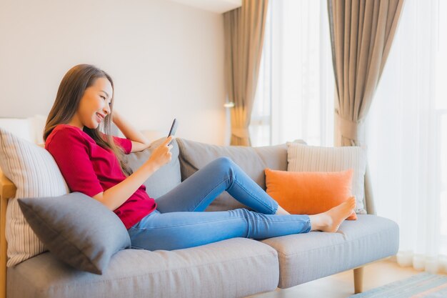 Retrato hermosa joven asiática utilizar teléfono móvil inteligente en el sofá