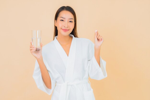 Retrato hermosa joven asiática con vaso de agua y píldora de drogas en beige