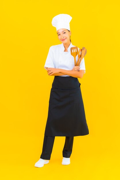 Retrato de una hermosa joven chef asiática con una espátula en un fondo aislado amarillo