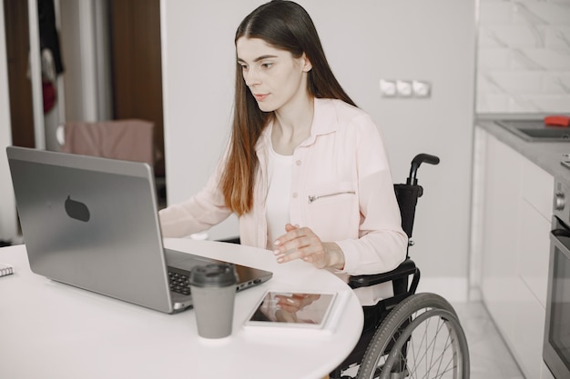 Retrato de una hermosa joven discapacitada en silla de ruedas, trabajando en casa en una computadora portátil, trabajo remoto.