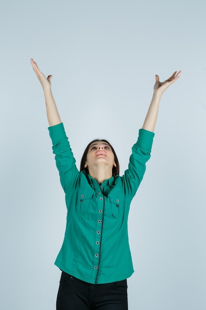 Foto gratuita retrato de hermosa joven estirando los brazos mientras mira hacia arriba con camisa verde y mirando agradecido vista frontal