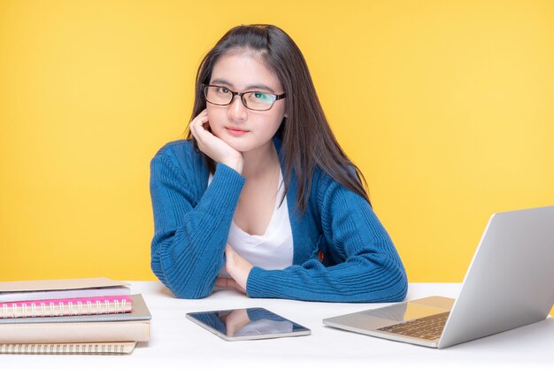 Retrato de una hermosa joven estudiando en la mesa con computadora portátil y portátil en casa - estudiando el sistema de e-learning en línea