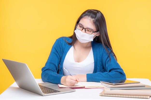 Retrato de una hermosa joven estudiando en la mesa con computadora portátil y portátil en casa - estudiando el sistema de e-learning en línea