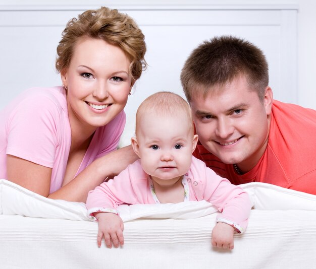 Retrato de la hermosa joven familia feliz acostado en la cama en casa