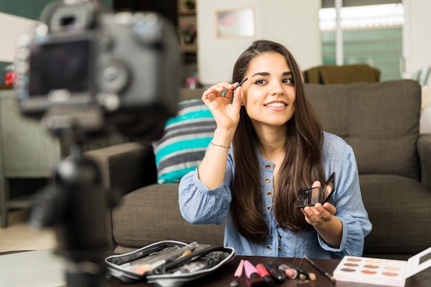 Retrato de una hermosa joven hispana dando consejos de belleza y maquillaje en cámara para su video blog