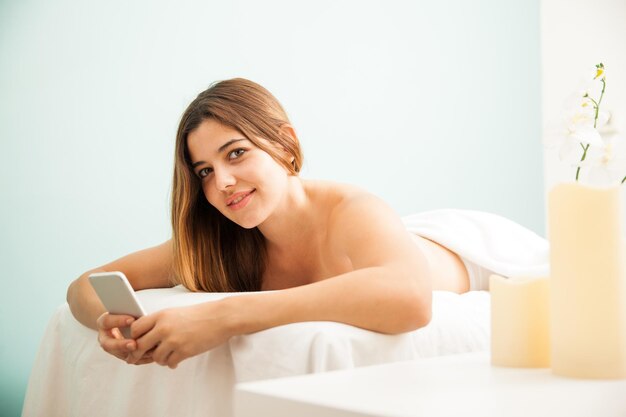 Retrato de una hermosa joven hispana usando su teléfono inteligente y enviando mensajes de texto mientras se relaja en un spa de salud