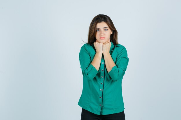 Retrato de hermosa joven manteniendo los puños debajo de la barbilla en camisa verde y mirando asustado vista frontal