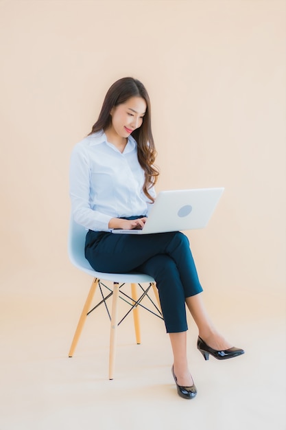 Retrato hermosa joven mujer asiática de negocios sentarse en una silla con ordenador portátil o teléfono inteligente para el trabajo