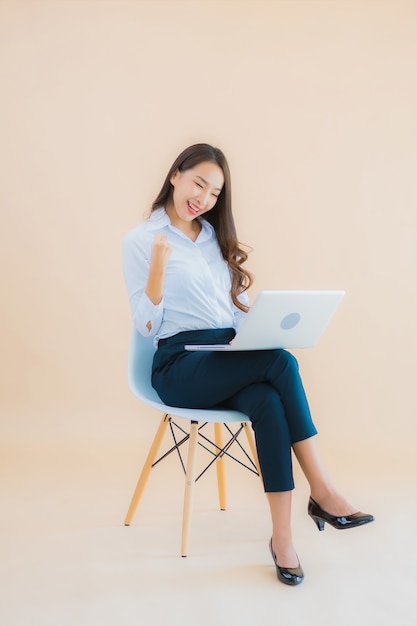 Retrato hermosa joven mujer asiática de negocios sentarse en una silla con ordenador portátil o teléfono inteligente para el trabajo