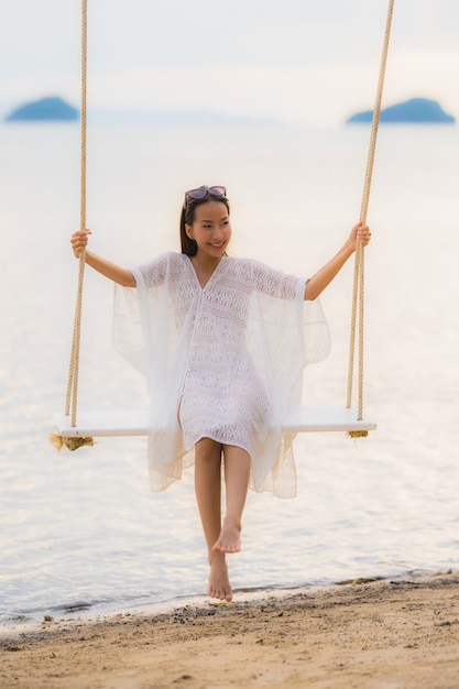 Retrato hermosa joven mujer asiática sentada en el columpio alrededor de la playa del mar océano para relajarse