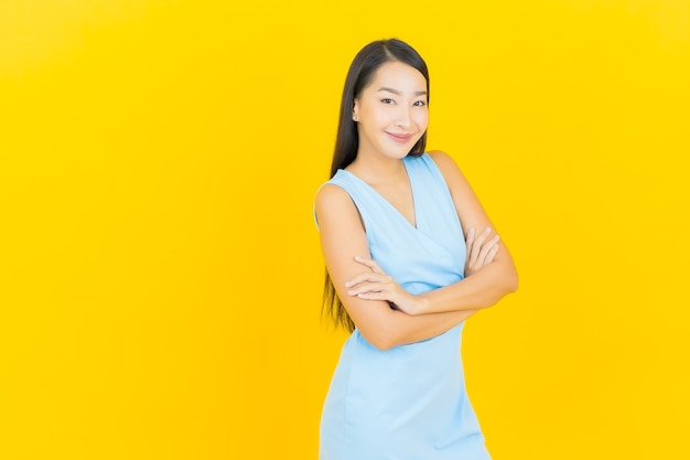 Retrato hermosa joven mujer asiática sonríe con acción en la pared de color amarillo