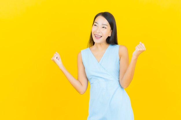 Retrato hermosa joven mujer asiática sonríe con acción en la pared de color amarillo