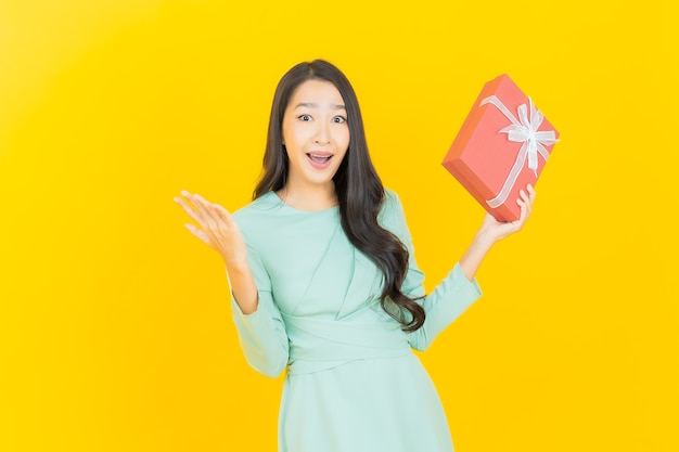 Retrato hermosa joven mujer asiática sonrisa con caja de regalo roja sobre amarillo
