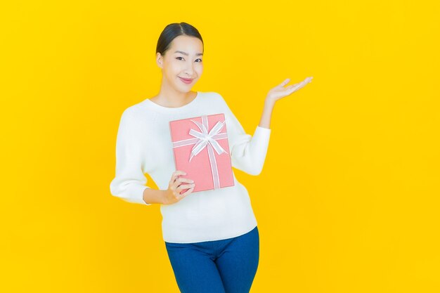 Retrato hermosa joven mujer asiática sonrisa con caja de regalo roja sobre amarillo