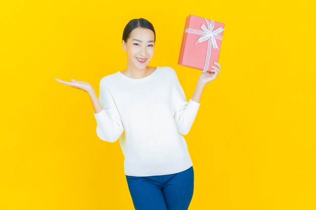 Retrato hermosa joven mujer asiática sonrisa con caja de regalo roja sobre amarillo