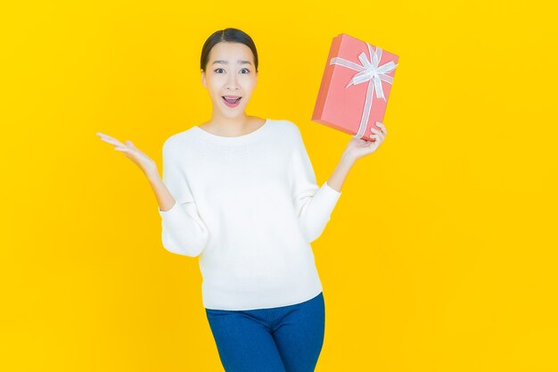 Retrato hermosa joven mujer asiática sonrisa con caja de regalo roja sobre amarillo