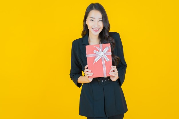 Retrato hermosa joven mujer asiática sonrisa con caja de regalo roja sobre amarillo