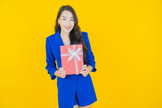 Retrato hermosa joven mujer asiática sonrisa con caja de regalo roja sobre amarillo