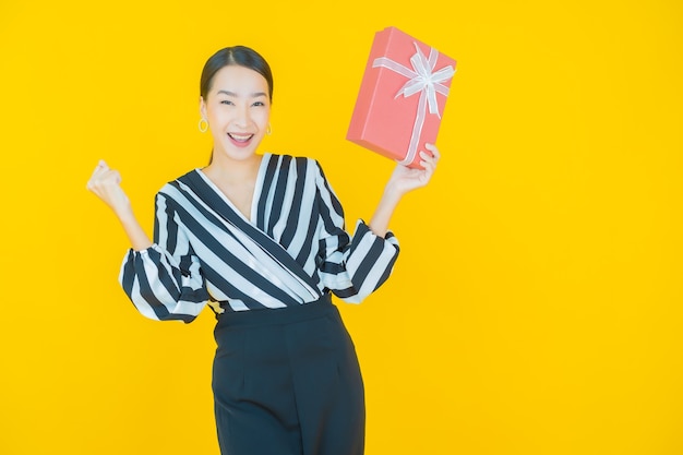 Retrato hermosa joven mujer asiática sonrisa con caja de regalo roja sobre amarillo