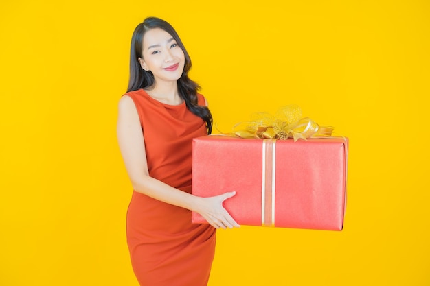 Retrato hermosa joven mujer asiática sonrisa con caja de regalo roja sobre amarillo