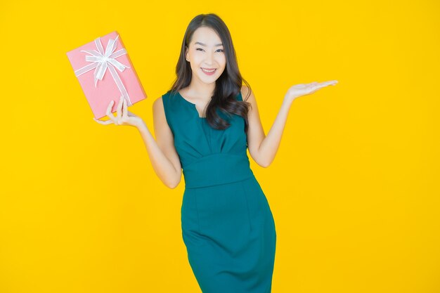 Retrato hermosa joven mujer asiática sonrisa con caja de regalo roja sobre amarillo