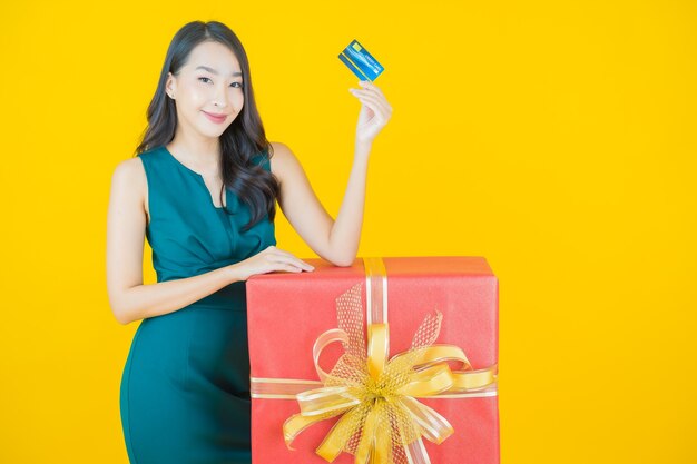 Retrato hermosa joven mujer asiática sonrisa con caja de regalo roja sobre amarillo