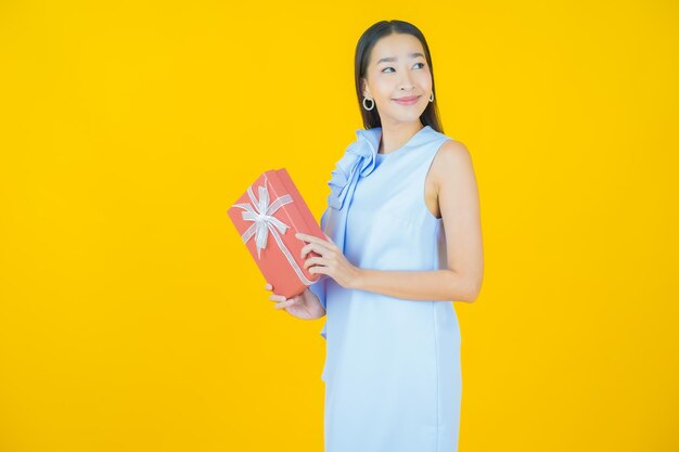 Retrato hermosa joven mujer asiática sonrisa con caja de regalo roja sobre amarillo