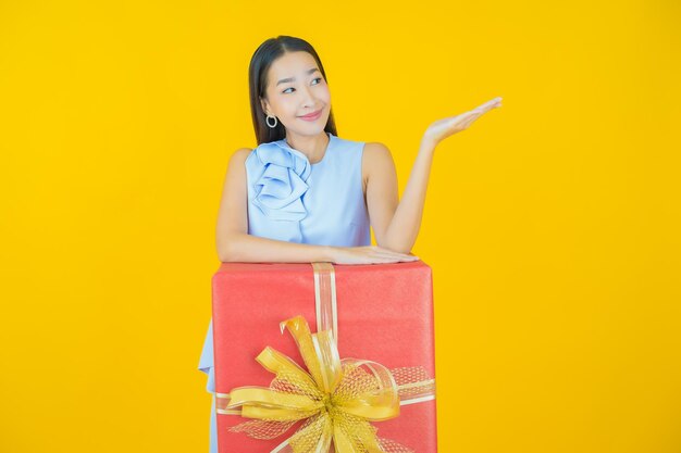 Retrato hermosa joven mujer asiática sonrisa con caja de regalo roja sobre amarillo