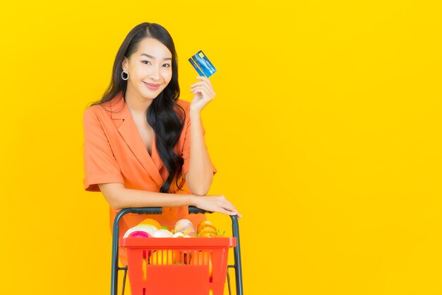 Retrato hermosa joven mujer asiática sonrisa con canasta de supermercado en amarillo