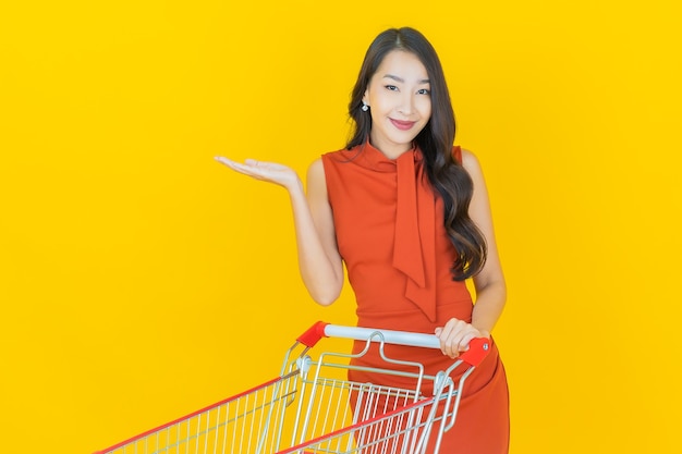 Retrato hermosa joven mujer asiática sonrisa con canasta de supermercado en amarillo