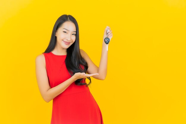 Retrato hermosa joven mujer asiática sonrisa con llave de coche en la pared amarilla