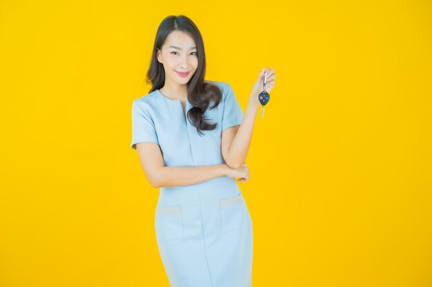 Retrato hermosa joven mujer asiática sonrisa con llave de coche sobre fondo de color amarillo